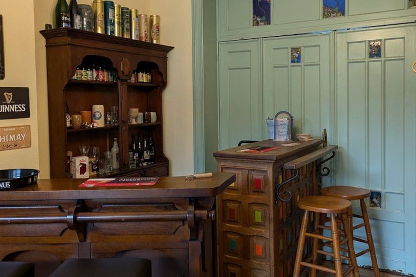 A bar with a wooden counter, stools, and a shelf with bottles. 2