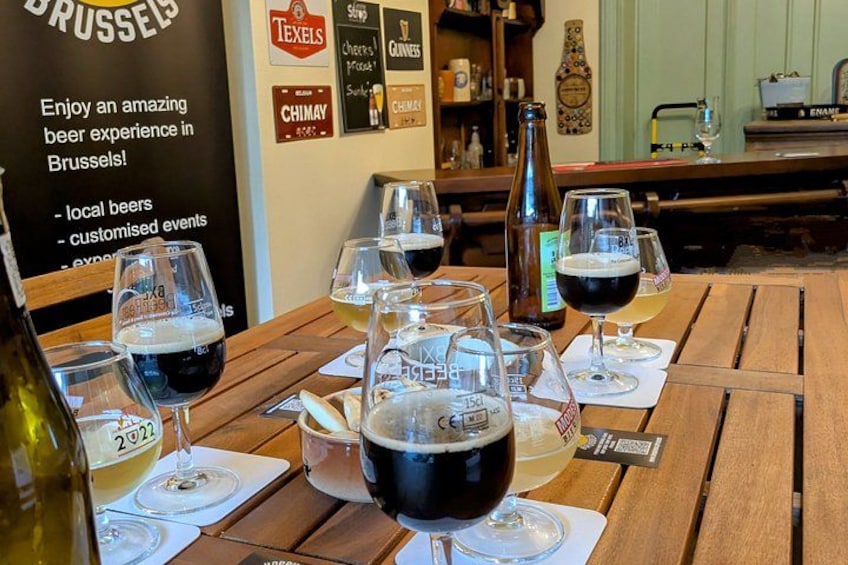 A wooden table with several glasses of beer, a bottle, and a sign about beer experience in Brussels. 1