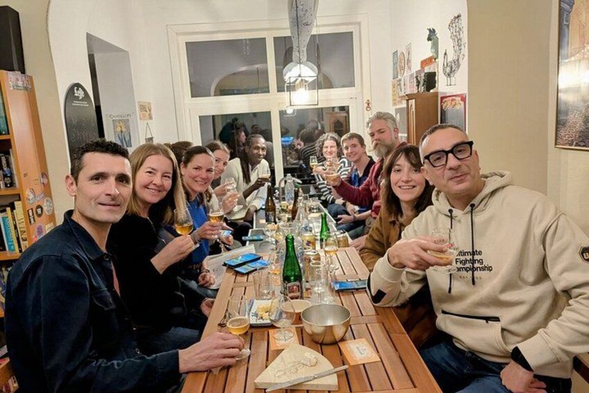 Un grupo de personas sentadas alrededor de una mesa de madera con botellas y vasos, en una habitación con estanterías y un ventanal. 2