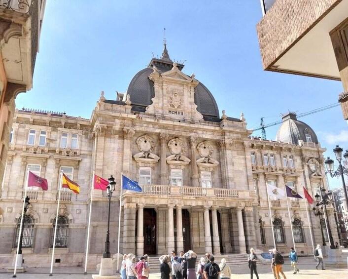 A historic building with a dome and columns, flags, and a crowd of people. 4