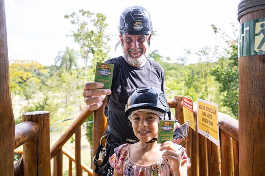 A person holding a card and a child holding a card, with a wooden railing and greenery in the background. 3