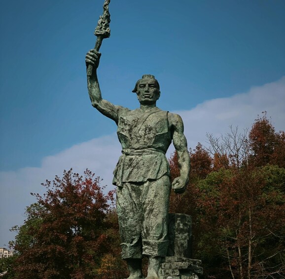 A statue of a figure holding a staff, set against a backdrop of trees and a clear sky. 2