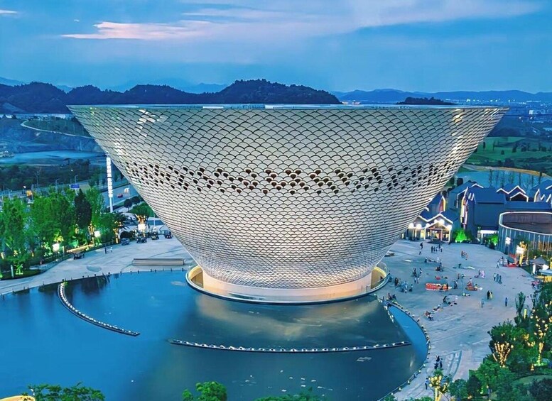 A large, spherical, metallic structure with a patterned surface, surrounded by a body of water and a landscaped area with trees and buildings. 1