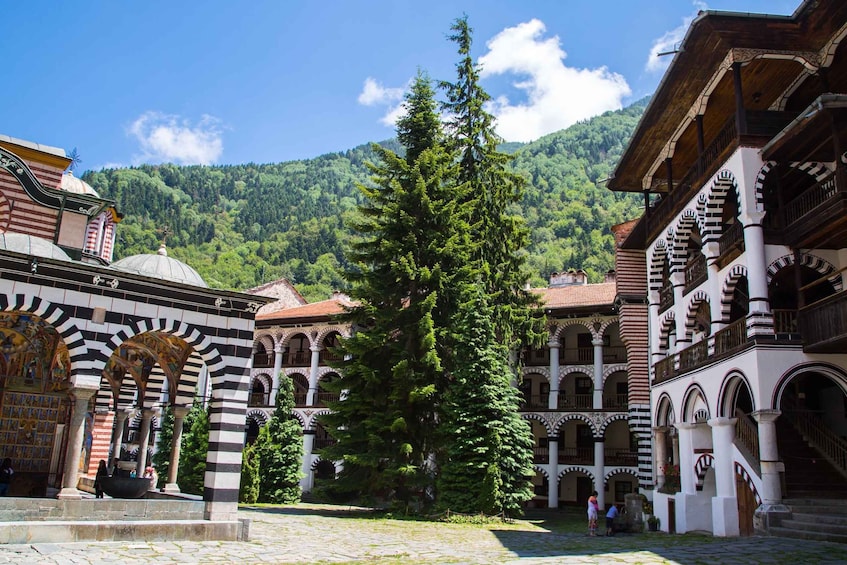 A historic courtyard with arches, a large tree, and mountainous backdrop. 4
