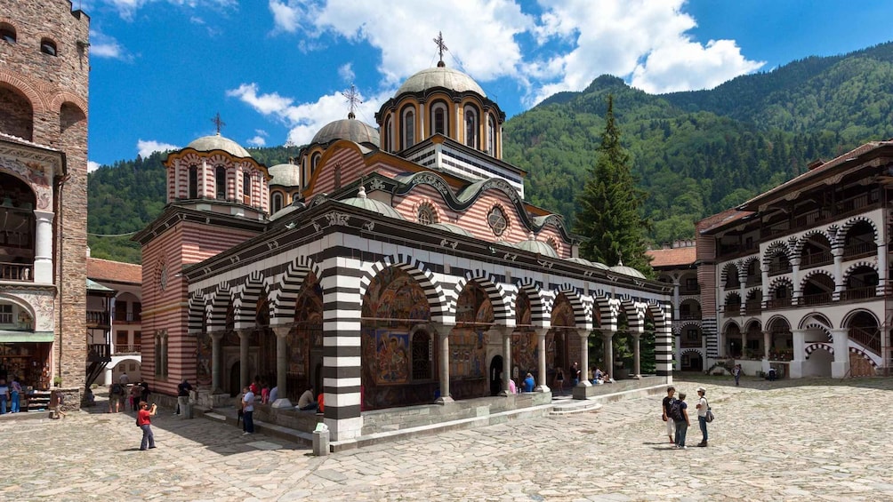 A historic church with multiple domes and arches, surrounded by a courtyard and visitors. 1