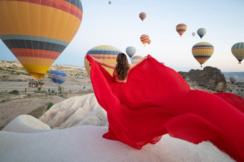 A person in a red dress lying on a white surface with hot air balloons in the background. 1