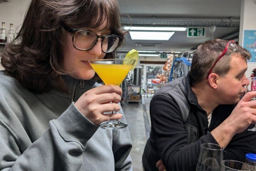 Twee personen zitten binnen, één houdt een geel drankje met een limoenpartje vast. 3