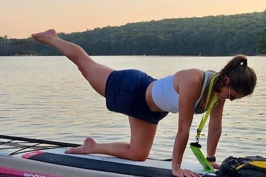 Una persona realizando una postura de yoga en un bote, con un lago tranquilo y árboles al fondo. 5