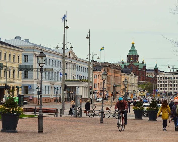 A city street with historic buildings, a cyclist, pedestrians, and a church with a green dome. 2
