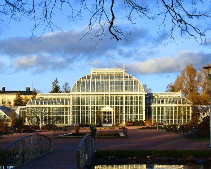 A large glass greenhouse with a dome roof, surrounded by a brick pathway and a small pond. 3
