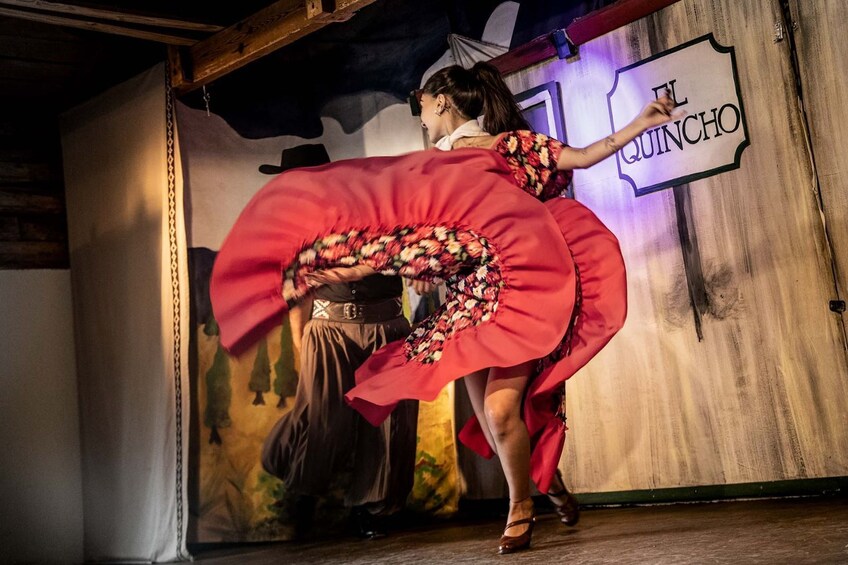 A person dancing in a red dress with a large skirt, in front of a sign that reads 'EL QUINCHO.' 3