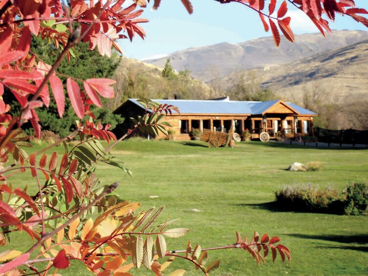 A rustic cabin with a blue roof, surrounded by a grassy field and red-leaved trees, with mountains in the background. 4