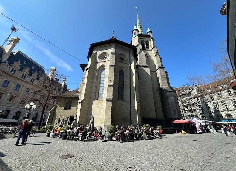 A historic church with a tall spire, surrounded by a cobblestone square with people and outdoor seating. 4