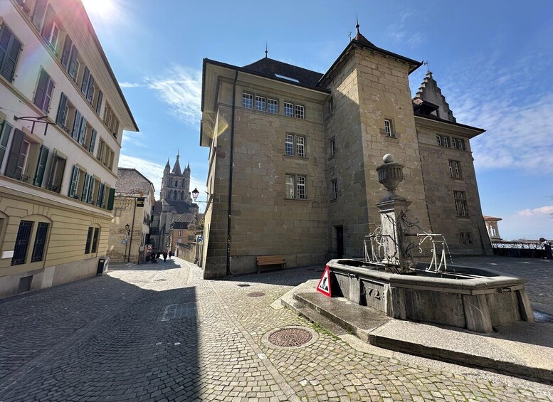 A cobblestone square with historic buildings, a fountain, and a church in the background. 3