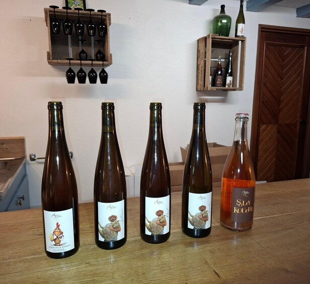 Four wine bottles with cartoon labels on a wooden table, a wine rack with glasses, and a door in the background. 1