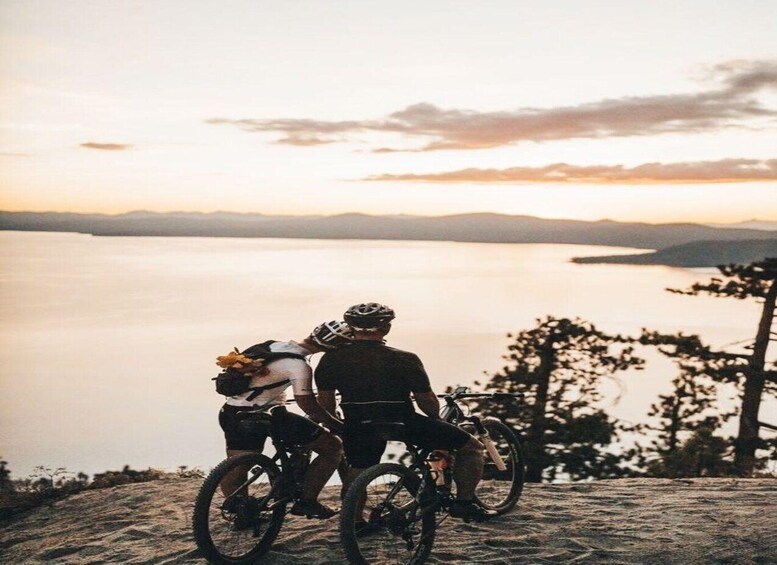 Two cyclists on a mountain trail overlooking a calm lake at sunset. 2