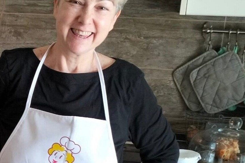 A person wearing a white apron with a cartoon character, standing in a kitchen with wooden walls and hanging kitchen utensils. 1