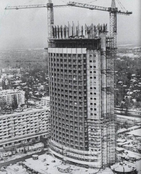 A tall building under construction with a crane, surrounded by other buildings and a snowy landscape. 4
