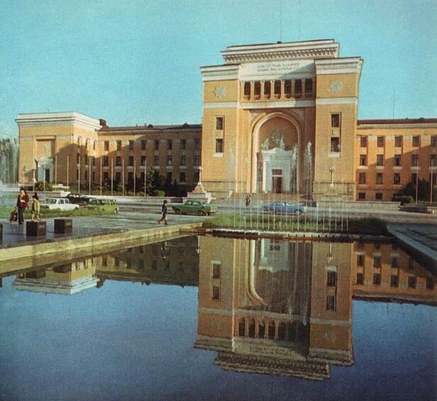 A large building with a central archway, surrounded by a reflective water feature and a parking lot. 3
