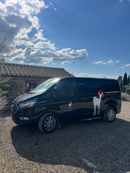 A black van parked in front of a stone building with a tiled roof, under a partly cloudy sky. 2
