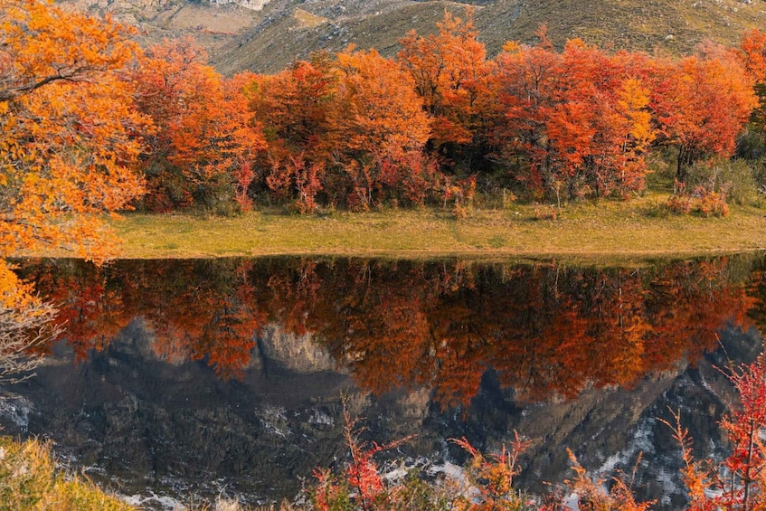 A lake reflecting autumn trees with a mountainous backdrop. 4