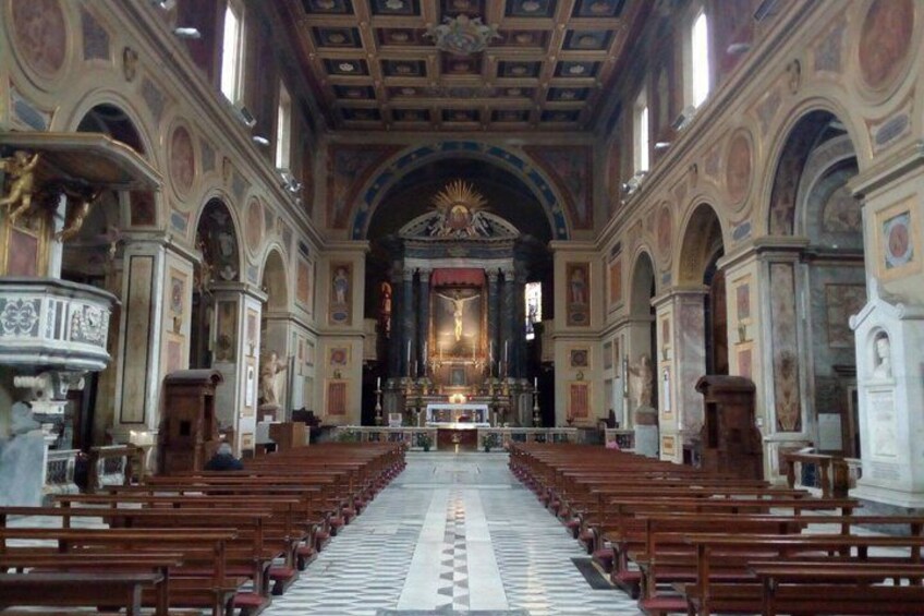 Interior de una iglesia con hileras de bancas de madera, un altar central y un techo abovedado con frescos. 2