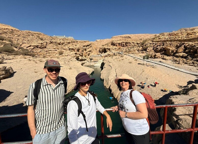Three people standing on a bridge over a water channel in a rocky landscape. 2