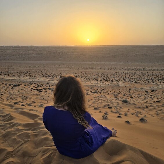A person sitting on sand dunes facing a sunset. 3
