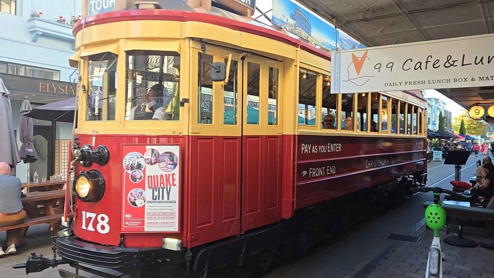 A vintage tram numbered 178 with a 'Quake City' advertisement, parked at a station with a '99 Cafe & Lounge' sign in the background. 2