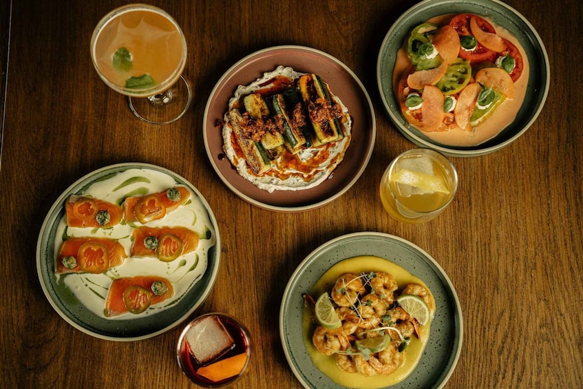 A variety of dishes on a wooden table, including grilled vegetables, shrimp, and a creamy soup. 1