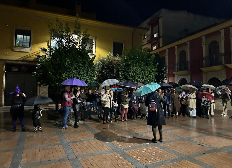 A nighttime outdoor gathering with people holding umbrellas, a yellow building, and trees in the background. 3