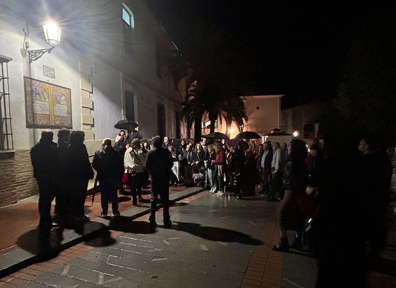 A nighttime outdoor gathering with people standing and walking on a street. 2
