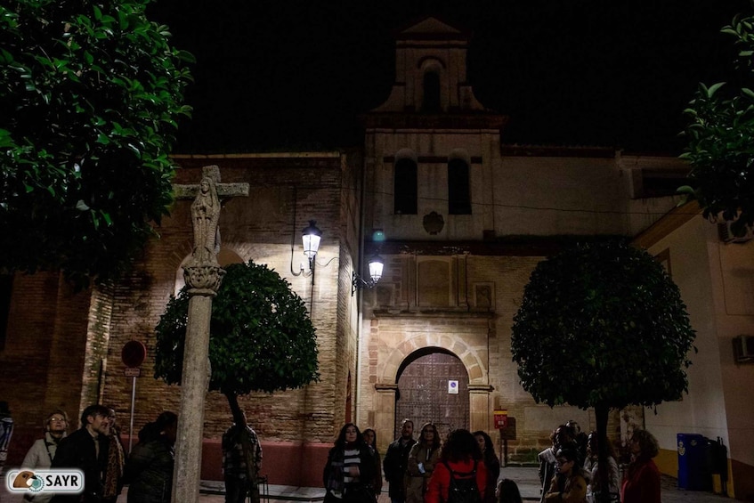 A nighttime scene with a group of people gathered around a historical building with a bell tower. 1