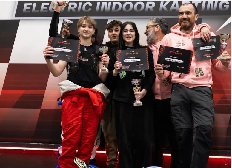 A group of people holding trophies in an indoor setting with a banner reading 'ELECTRIC INDOR KASTING'. 2