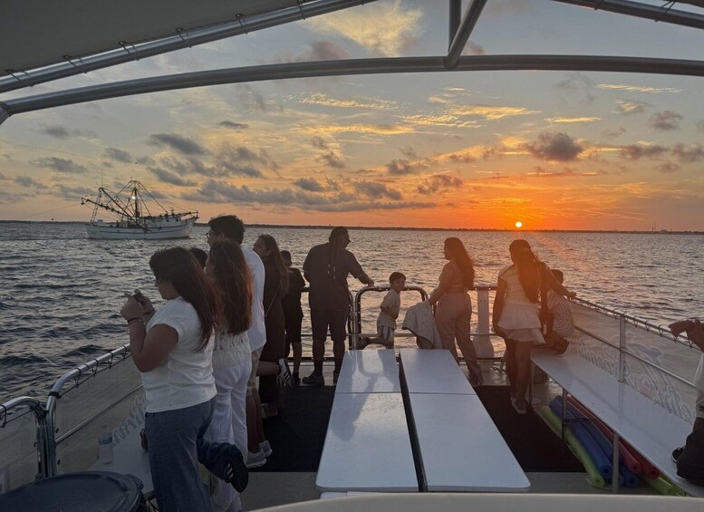 A group of people on a boat during sunset, with a fishing boat in the background. 1