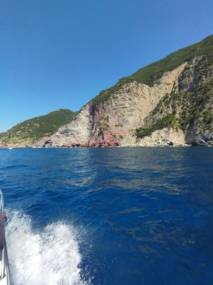 A boat on a clear blue sea with a rocky coastline and green hills in the background. 3