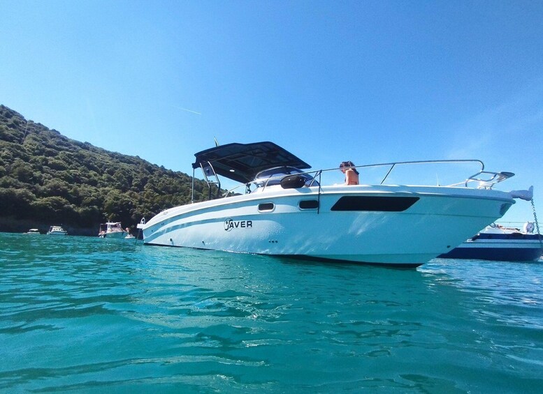 A white boat named 'JAVER' on clear turquoise water with a forested hill in the background. 1