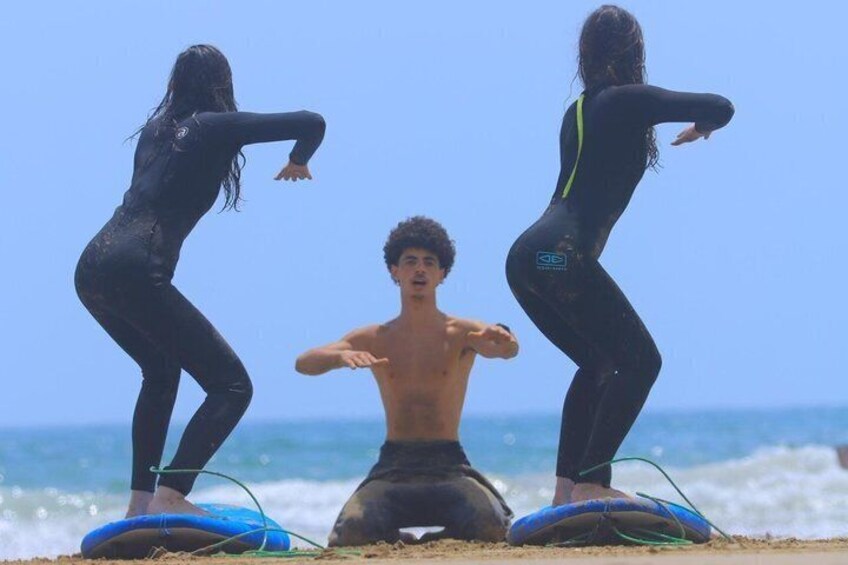 Drei Personen auf Surfbrettern am Strand, im Hintergrund das Meer. 3