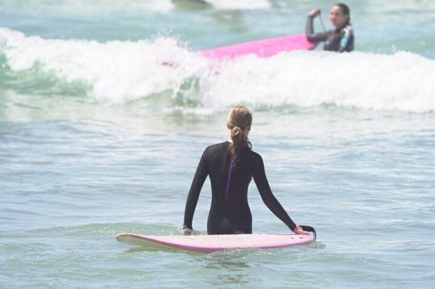 A person in a wetsuit standing on a pink surfboard in the ocean, with waves in the background. 5