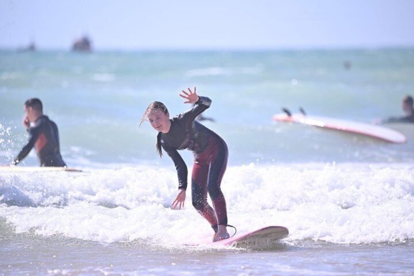A person surfing on a wave with a pink surfboard, another person in the background, and a ship in the distance. 1