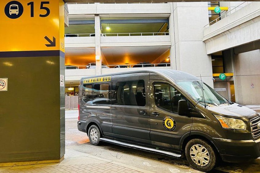 A grey van with 'The Fairy Bus' written on the side parked near a building with a parking sign. 2