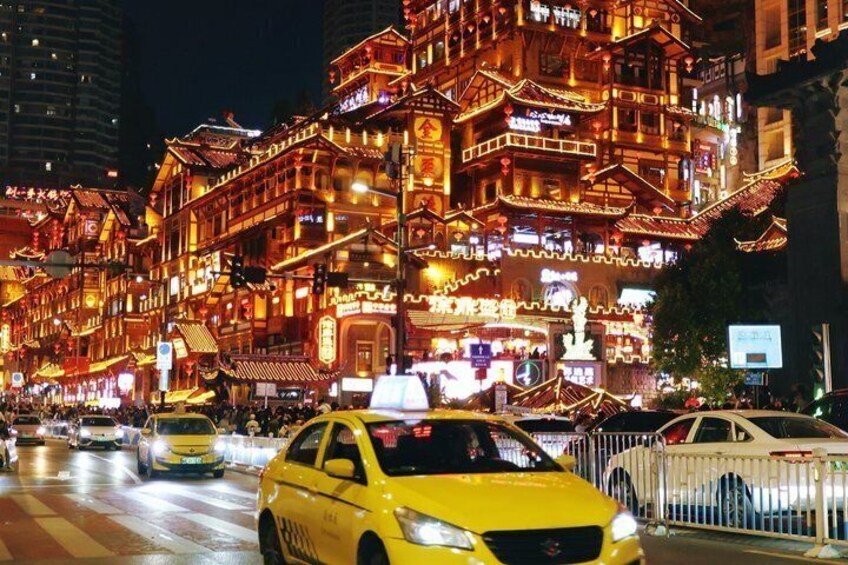 A brightly lit traditional building with multiple balconies and a busy street with yellow taxis. 1