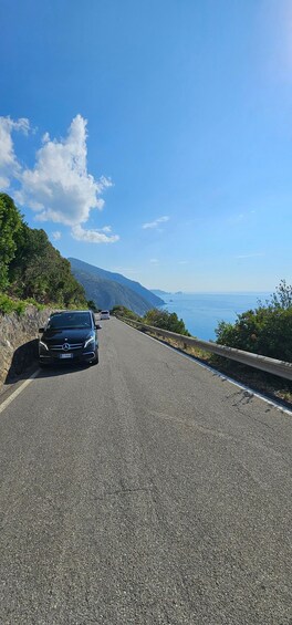 A black car on a winding mountain road with a clear blue sky and ocean in the distance. 3