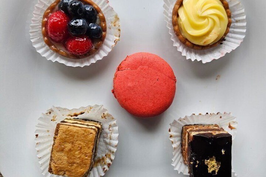 Five desserts in paper cups: two with berries, one with a red macaron, one with a yellow swirl, and two with layered cakes. 4
