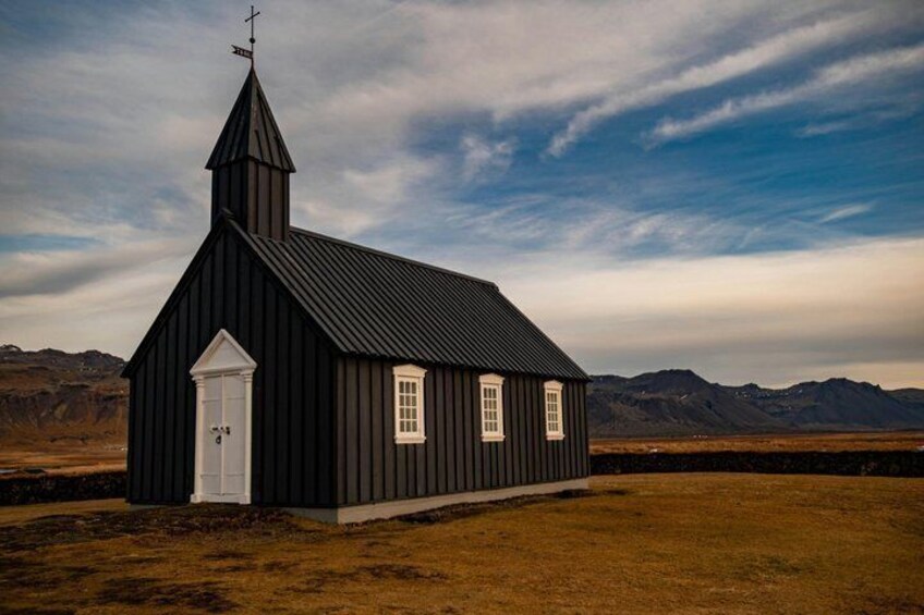 A black church with a white door and windows, set against a mountainous backdrop. 2