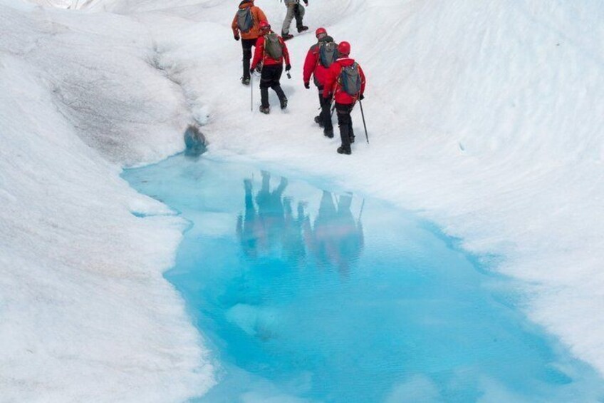 Un gruppo di escursionisti che sale lungo un pendio innevato con un corpo d'acqua blu e riflettente. 1