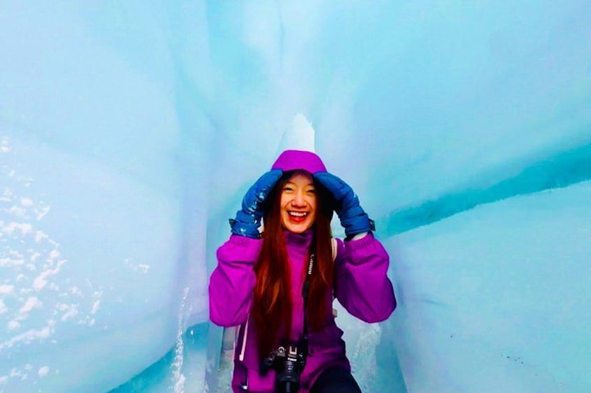 A person in a purple jacket and blue gloves inside an ice cave. 4