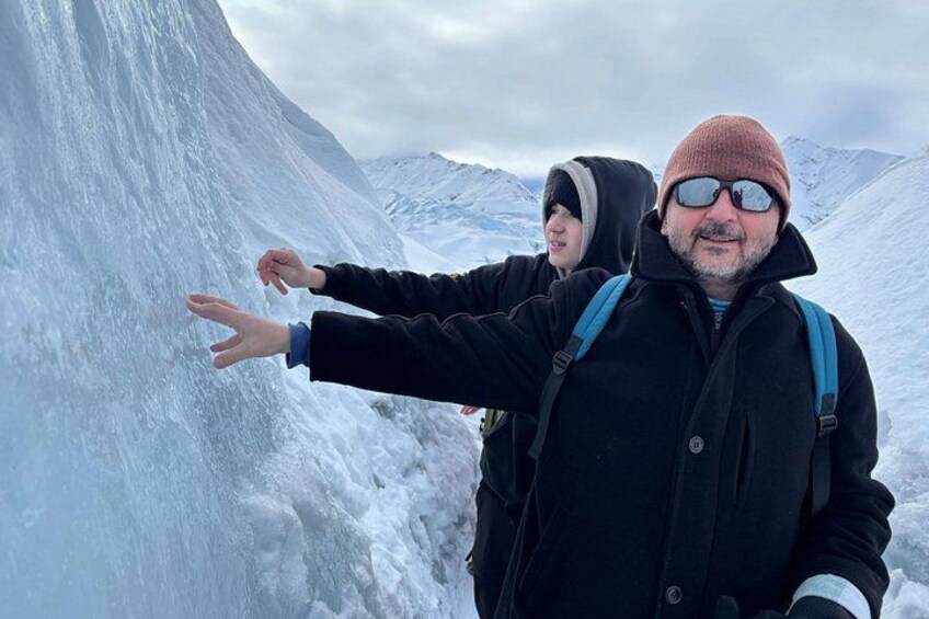 Two people standing in a snowy mountainous area with a large ice formation. 3