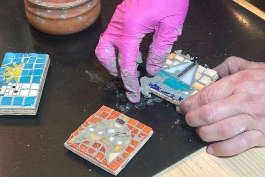 Una persona con guanti rosa che lavora su una piastrella di mosaico con un pezzo rotto. 3
