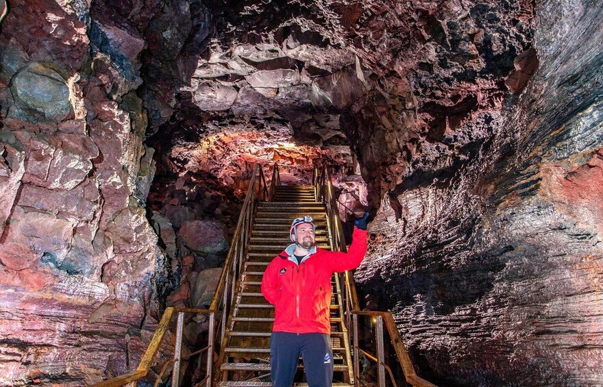 A person in a red jacket standing on a metal staircase inside a cave with rocky walls. 2